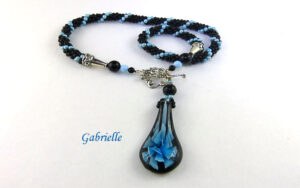 Ce collier de perles est de création et conception uniques. Il mesure 56 cm le pendentif de verre 6 cm Le fermoir est idéal pour les personnes qui ont des douleurs aux mains. Cette création a été fait avec des perles noires et insertion de perles bleues. Un certificat confirme son unicité. Beau collier de perles viendra compléter n’importe quelle tenue, conviens pour le bureau et pour la soirée. C’est une excellente idée cadeau pour anniversaire ou toute autre occasion. Il mesure 56 cm le pendentif de verre 6 cm