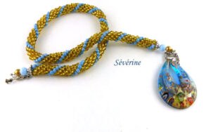 Collier de perles Sérévine. Composé de perles or avec insertion de perles bleue pale le tout terminé par un petit embout de métal argent, une grosse perle bleu et une autre perle or. Il se termine par un fermoir décoratif a bascule . Son pendentif est en forme de larme de couleur bleu avec or. Pièce unique un certificat est émis. Le collier mesure 52 cm fermoir inclus, son pendentif 5 cm.