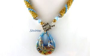 Collier de perles Sérévine. Composé de perles or avec insertion de perles bleue pale le tout terminé par un petit embout de métal argent, une grosse perle bleu et une autre perle or. Il se termine par un fermoir décoratif a bascule . Son pendentif est en forme de larme de couleur bleu avec or. Pièce unique un certificat est émis. Le collier mesure 52 cm fermoir inclus, son pendentif 5 cm.