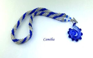 Collier de perles Camélia.Fabriqué dans la technique de crochet de perle, avec des perles de verre transparentes et des perles bleues. Le tout terminé par un petit embout de métal argent ainsi que deux perles bleues et deux perles transparentes. Son fermoir est a bascule et très décoratif. Son pendentif est bleu avec la forme d'une crevette. Longueur: 58 cm pendentif: 6 cm www.metiersdar-cadeaux.com