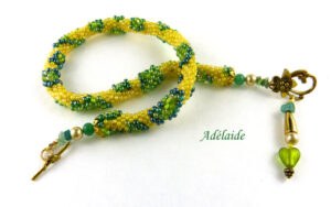 Collier de perles Adélaide. Il est composé de perles jaunes avec insertion de perles de deux tons de vert il est terminé par des embouts en métal or ainsi que 4 petites perles vertes. Le tout terminé. par un fermoir a basxule or qui est très décoratif Longueur du collier : 48 cm Son pendentif:5 cm et composé de deux petites perles jaune ainsi qu'une perle verte et un cône or ainsi qu'un petit coeur de verre vert. www.metiersdart-cadeaux.com