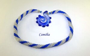 Collier de perles Camélia.Fabriqué dans la technique de crochet de perle, avec des perles de verre transparentes et des perles bleues. Le tout terminé par un petit embout de métal argent ainsi que deux perles bleues et deux perles transparentes. Son fermoir est a bascule et très décoratif. Son pendentif est bleu avec la forme d'une crevette. Longueur: 58 cm pendentif: 6 cm