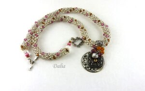 Collier de perles Dalia. Collier de perles fait avec des perles rocaille en verre clair et insertion de perles or et rose. Pour faire ce collier, des perles rocaille ont été utilisées et terminées par des cônes métal argent ainsi que des perles blanches, rose, et brunes d'une longueur de 57 cm Le pendentif est composé d'une base carrée avec des perles rose et jaune, sa longueur est de 3 cmwww.metiersdart-cadeaux.com