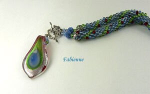 .Collier de perles Fabienne est composé de Les couleurs sont bleu vert et des insertions de rouge. terminé par des embouts de métal argent une grosse perle Shambala bleu et deux petites perles et un magnifique fermoir a bascule décoratif argent. Son pendentif est en forme de larme avec des couleurs verte, bleu et rouge.Sa longueur est de 55 cm. Son pendentif est de 5 cmwww.metiersdart-cadeaux.com