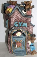 La tirelire en forme de GYM avec des petites briques rose et la porte bleu et la porte est bleu, il y a des petits oursons sur le toit et un autre a la porte vient avec son cadenas et sa clé. Elle mesure26 cm X 13.5 cm ou 10″ X 5″. www.metiersdart-cadeaux.com