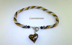 Collier de perles Laurentienne, Sa conception se compose de perles de verre transparentes avec insertion de perles or et noires le tout terminé par en embout de métal et une perle noire, transparente et jaune. Son fermoir argent très décoratif et a bascule il mesure 48 cm. Magnifique pendentif en forme de coeur de couleur or noir et transparent il mesure 3 cm 1/2 pendentif est de 3 cm 1/2