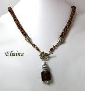 Collier de perles Elmina, Ce collier est composé de perles brunes avec insertion de perles or.Il est terminé par une cone argent et des petites perles brunes et or. Il mesure: 59cm son pendentif est carré de couleur brune et or et il mesure 6cm.. Le fermoir est a bascule en argent