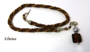 Collier de perles Elmina Ce collier est composé de perles brunes avec insertion de perles or.Il est terminé par une cone argent et des petites perles  brunes et or. Il mesure: 59cm son pendentif est carré de couleur brune et or  et il mesure 6cm..  Le fermoir est a bascule en argent