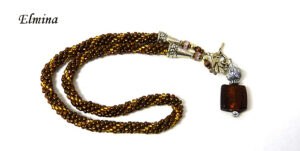Collier de perles Elmina, Ce collier est composé de perles brunes avec insertion de perles or.Il est terminé par une cone argent et des petites perles  brunes et or. Il mesure: 59cm son pendentif est carré de couleur brune et or  et il mesure 6cm..  Le fermoir est a bascule en argent