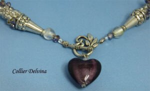 Collier de perles transparent blanc avec insertion de perles cubiques mauve terminé par un coeur mauve. Ce collier à un fermoir décoratif il facilite l'attachement au collier.
