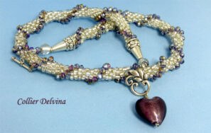 Collier de perles transparent blanc avec insertion de perles cubiques mauve terminé par un coeur mauve. Ce collier à un fermoir décoratif il facilite l'attachement au collier.