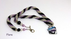 Collier de perles de verre Flore, perles transparente avec insertion de perles noires et lilas. Le collier de perles mesure 55 cm. Son pendentif 3 cm. Son pendentif est carrée de couleur transparent, noire et lilas il est une création unique d’une artisane, Son fermoir est argent a bascule argent. Les embouts du collier sont terminé par un cône argent.