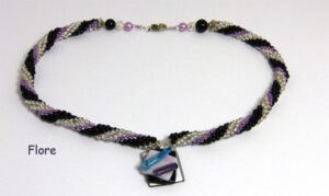 Collier de perles de verre Flore, perles transparente avec insertion de perles noires et lilas. Le collier de perles mesure 55 cm. Son pendentif 3 cm. Son pendentif est carrée de couleur transparent, noire et lilas il est une création unique d’une artisane, Son fermoir est argent a bascule argent. Les embouts du collier sont terminé par un cône argent.