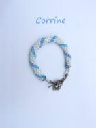 Bracelet de perles blanches avec insertion de perles bleues le tout terminé avec un embout de métal argent et un fermoir a bascule le tout terminé par une chaine de sécurité il mesure Il mesure 15 cm.r