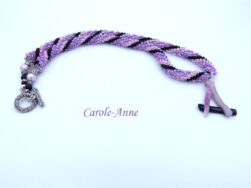 Collier crocheté avec perles de verre de couleurs mauve, rose et noires. La pièce de verre central est une création unique d’une artiste québécoise, il a la forme de A soit deux bandes de lilas et la barre du A est noire. Le collier est terminé Le fermoir a bascule mesure 55 cm Longueur 53 cm ce collier est crocheté et terminé avec un embout de métal argent et de petites perles blanches, et noires, un fermoir a bascule rond argent termine le tout.