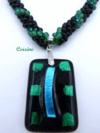 Sa conception a été faite avec des perles noires ainsi que des perles vertes et noires, il est terminé par une pièce de métal argent et des perles noires et vertes. Longueur:54 cm Pendentif: est en forme de rectangle av. fond noir et de petits carrés de vert et un rectangle bleu. 5 cm