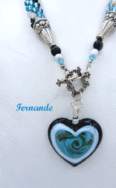 Collier de  perles Fernande Ce collier de perles de verre est fait avec des perles verre bleues et insertion de perles noires et blanches le tout terminé par un cone argent  et une petite perles noire, une autre perle blanche et ter miné par une perle bleu. Le fermoir décoratif est très facile à manipuler il est a bascule.  Le pendentif est en forme de coeur avec un contour noir et blanc et dans le centre du bleu. Longueur : 57 cm incluant le fermoir. Diamètre : 4cm Pendentif: 5 cm