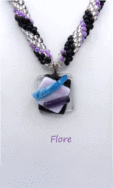 Collier de perles Flore est composé de perles de verre transparente et des perles noire ainsi que des perles mauve. Son pendentif est carré et est en verre transparent avec insertion de perle noire plus une autre perles carré mauve et deux petites languettes de verre une bleu et l'aitre noire. Le tout est terminé par un fermoir a bascuel. Le collier de perles mesure 55 cm. Son pendentif 3 cm.