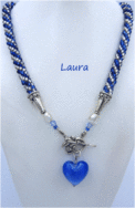 Collier de perles Laura. Il est composé de perles bleues avec insertion de perles transparentes le tout terminé par des cones de métal argent et deux autre grosses perles ensuite deux petites perles bleues il est terminé par un fermoir décoratif a bascule et un magnifique coeur bleu . Le collier fait environ 60 cm de long. Il est fait de perles de rocaille bleue et verre transparent. Son pendentif mesure 3 cm