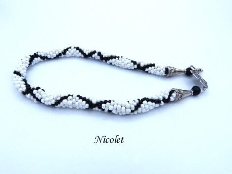 Collier de perles Nicolet il est composé de perles blanches avec insertion de perles noires en diagonales Il a un fermoir a bascule argent Il mesure 50 cm le pendentif 6 cm. Un diamètre de 3 1/2 cm