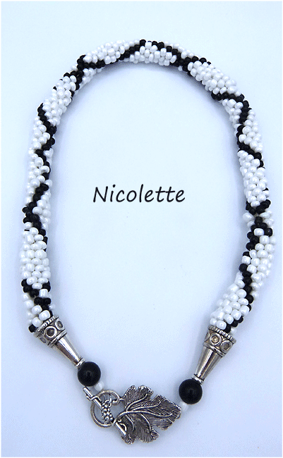 collier de perles Nicolette est un collier de perles blanches avec insertion de perles noires qui forme une X. Il est terminé par des embouts de métal argent et une grosse perles chamballa et un fermoir a bascule en forme de feuille. Il vient avec son certificat Il mesure 50 cm le pendentif 6 cm Un diamètre de 3 1/2 cm