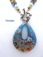 Collier de perles Sérévine. Composé de perles or avec insertion de perles bleue pale le tout terminé par un petit embout de métal argent, une grosse perle bleu et une autre perle or. Il se termine par un fermoir décoratif a bascule . Son pendentif est en forme de larme de couleur bleu avec or. Pièce unique un certificat est émis. Le collier mesure 52 cm fermoir inclus, son pendentif 5 cm.
