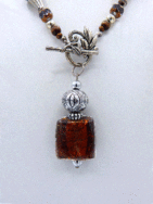 Ce collier est composé de perles brunes avec insertion de perles or.Il est terminé par une cone argent et des petites perles brunes et or. Il mesure: 59cm son pendentif est carré de couleur brune et or et il mesure 6cm.. Le fermoir est a bascule en argent