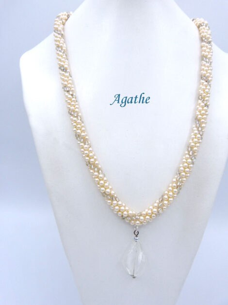 Collier de perles Agathe est composé de perles blanches avec insertion de perles transparente. Il est terminé par un embout de métal argent une grosse perle transparente et une petite perle blanche. Son fermoir a bascule est en argent décoratif.  Il mesure: 61 cm Son pendentif est en verre transparent. Son pendentif: 4 cm