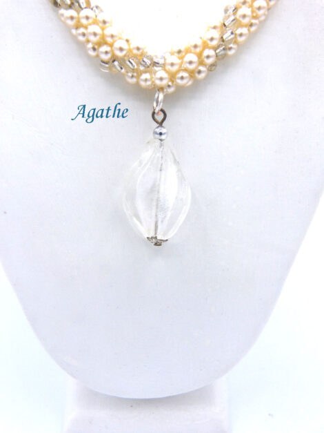 Collier de perles Agathe est composé de perles blanches avec insertion de perles transparente. Il est terminé par un embout de métal argent une grosse perle transparente et une petite perle blanche. Son fermoir a bascule est en argent décoratif. Il mesure: 61 cm Son pendentif est en verre transparent. Son pendentif: 4 cm