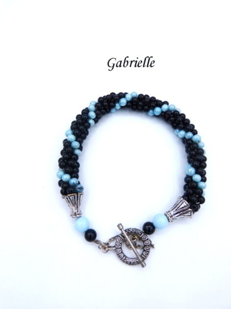 Bracelet de perles de verre Gabrielle. Ce bracelet est composé de perles noires avec insertion de perles bleue le tout terminé par des embouts de métal argent et une perle bleue et une autre perle noire. Son fermoir est a bascule avec une chaîne de sécurité. Ce bracelet mesure 22 cm.