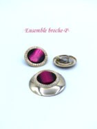 Ensemble boucles d'oreilles a pinces et une broche avec base en or le tout terminé par une perle rose miroitant noire.