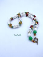 Collier de perles blanches avec des perles rouge, jaune et vert qui forme des fleurs sur le collier il est terminé par des embouts de étal argent , une grosse perle blanche et une grosse perle verte et deux petites perles or et rouge. Son fermoir décoratif est à bascule en argent. Il mesure 57 cm