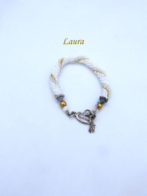 Magnifique bracelet de perle Laura Il est composé de petites perles blanches avec insertion de perles or et de perles transparentes. le tout terminé par des embouts de métal argent et une grosse perle or et une autre blanche. Il a un fermoir à bacul en forme de coeur et une chaînette de sécurité. Il mesure 17 cm