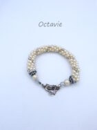 Ce bracelet  se compose de fines perles blanches avec insertion de perles de verre transparentes le tout est terminé par un embout de couleur argent et une grosse perle blanche et une autre petite perle transparente. Ce bracelet est avec un fermoir à bascule en forme de coeur et possède une chaîne de sécurité. Il mesure 19 cm.