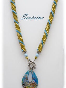 Le collier de perles que nous proposons est un véritable bijou de raffinement et d’originalité. Les perles tchèques, crochetées avec soin, arborent des nuances d’or et de bleu, rehaussées de vert et de noir pour un contraste élégant. Le pendentif en verre bleu-or est captivant, conférant une touche unique. Confortable et léger, il se ferme par un fermoir à bascule pratique. Idéal pour toute occasion, ce collier de 52 cm est livré avec un certificat d’authenticité, assurant qualité et unicité. Un bijou parfait pour sublimer chaque femme.