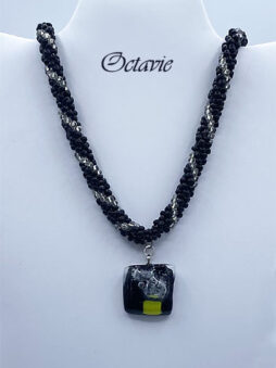 Collier de perles de verre noir avec iinsertion de perles transparentes, le tout terminé avec des petits cones argent une grosse perle ovale et un fermoir a bascule aussi très décoratif. pendentif qui est aussi une création unique d’une artiste québécoise. il est carré noire avec des insertions de verre transparent et un petit peu de vert